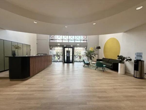 Moderne entreehal aan de Arnhemse Bovenweg met zithoek, receptiebalie en glazen draaideur.